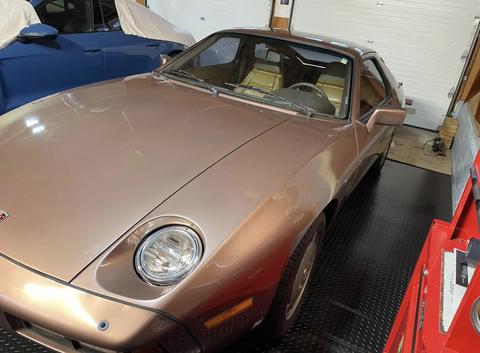 A bronze 1983 Porsche 928 with a sleek design and distinctive front headlights parked in a garage