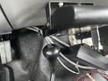 The gear shift lever of a 2003 Ford F-450 SD with a black knob and a textured surface visible amidst wiring and equipment in the vehicle's interior