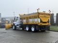 A 2016 International 7400 truck equipped with a yellow salt spreader and a front plow attachment