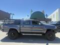A 2010 Toyota Tacoma in gray with a black grille and oversized tires is parked, featuring an open bed and a bed cover with cargo racks on the side