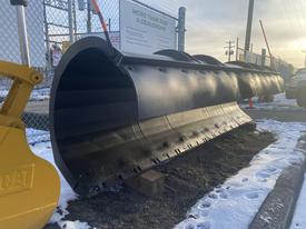 A black 2000 plow with a 12-foot attachment designed for snow removal with a curved shape and multiple horizontal ridges
