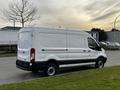 A white 2017 Ford Transit cargo van parked along the curb showing its side and rear profiles with a simple design and no visible branding