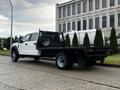 A white 2021 Ford F-550 with a flatbed and mounted spare tire parked on a concrete surface