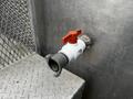 A metallic valve with a red handle attached to a silver pipe on a textured surface