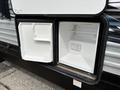 A partially open camper refrigerator revealing empty shelves and a small freezer compartment inside