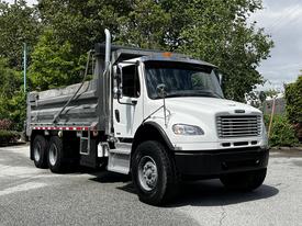 A white 2010 Freightliner M2 106 dump truck with a gray bed and large wheels parked at an angle
