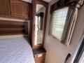 Interior view of a 2013 Outdoor Wind River showing a bed with a white mattress and a wooden cabinet with a mirror and a small countertop