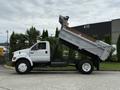 A white 2004 Ford F-750 dump truck with its bed raised for unloading materials