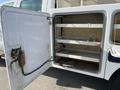 A 2015 Ford F-450 SD truck with an open door revealing an empty storage compartment featuring metal shelving and a clean interior surface