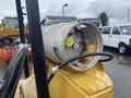 A close-up of a propane tank attached to a forklift with valves and a gauge visible