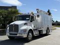 A white 2009 Kenworth T270 truck with a raised utility platform and multiple amber lights on top parked on a street