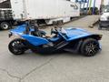 A blue 2020 Polaris SlingShot is parked with a sleek design featuring a streamlined body and two seats visible in the foreground