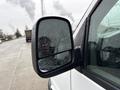 A close-up of the side mirror of a white 2014 GMC Savana with raindrops on the glass