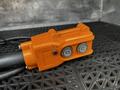 An orange control box with two buttons and a red indicator light connected to a gray cable