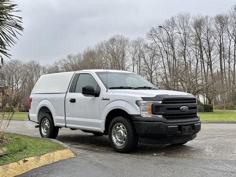 A white 2018 Ford F-150 with a pickup truck bed cover parked on a road