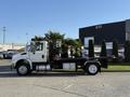 A 2017 International 4300 truck with a flatbed design is shown from the side featuring a white cab and black flatbed with visible wheels and metal attachments
