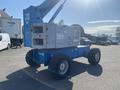 A blue 1997 Genie S-65 4X4 aerial work platform with large wheels and an extended boom in the upright position