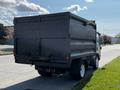 A 2016 Isuzu NPR truck facing away with a black dump bed and white wheels parked on a street