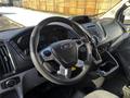 A 2018 Ford Transit interior featuring a steering wheel with controls a digital dashboard and a center console with various buttons and knobs