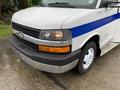 A 2015 Chevrolet Express van with a white body and blue stripe featuring a black front grille and an amber turn signal light