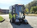 A 2015 Tennant 636 Green Machine street sweeper with a compact design featuring two front brushes and a large glass cab for improved visibility