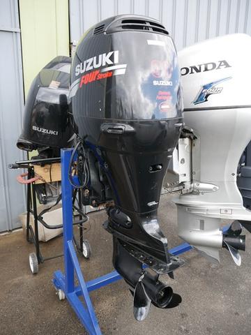 A Suzuki outboard motor engine mounted on a blue stand with a sleek black design and visible propeller