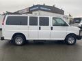 A white 2012 Chevrolet Express van with sliding side doors and chrome wheels captured from the side