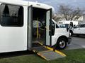 A white 2015 Chevrolet Express bus with open double doors and a yellow wheelchair ramp extended outward