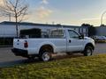 A white 2012 Ford F-250 pickup truck with a flatbed and ladder rack on the back parked on the street