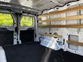 Interior view of a 2023 Ford Transit van showing empty cargo space with wooden shelves installed on the walls and a black rubber floor mat
