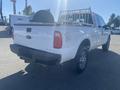 A 2014 Ford F-250 SD truck with a white exterior and a bed rack is parked with its tailgate open and a green object visible in the truck bed