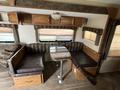 Interior view of a 2013 Outdoor Wind River with a seating area featuring a brown patterned couch and a table surrounded by cushioned benches