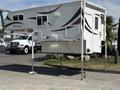 A 2018 Westland Travelaire truck camper features a sleek white exterior with decorative graphics and is supported by metallic legs for stability