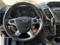 A steering wheel with the Ford logo and various controls attached depicted from a driver's perspective inside a 2018 Ford Transit