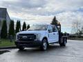 A white 2017 Ford F-350 SD truck with a flatbed and a black mesh side rack parked on a paved surface