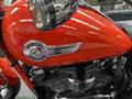 A close-up of a 2024 Harley Davidson Fat Boy motorcycle featuring a shiny red body and chrome details including a prominent Harley Davidson emblem