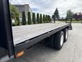 A 1998 Freightliner FL80 flatbed truck with a wooden deck and two rear axles is displayed in the foreground