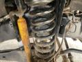 Close-up of a suspension system for a 2015 Ford F-550 featuring a coil spring and shock absorber with visible rust and wear on the components