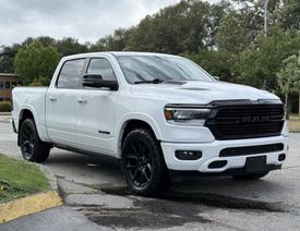 A white 2021 RAM 1500 pickup truck with black wheels and aggressive front grille design parked on a paved surface