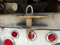 A close-up of a rusty hitch mounted on a steel dump trailer featuring a circular loop on top and a keyhole beneath it with red reflectors visible on the trailer's surface