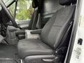 Two black cloth seats of a 2017 Mercedes-Benz Sprinter are positioned in the foreground with armrests and seatbelts visible
