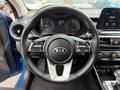 The image shows the steering wheel of a 2021 Kia Forte featuring controls for multimedia and vehicle settings with a Kia emblem at the center