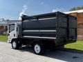 A 2016 Isuzu NPR with a black dump truck bed and white wheels parked on a paved surface