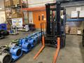 A 2021 Toyota Fork Lift with a black body and orange forks positioned in front of several blue industrial fans