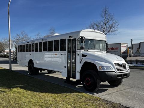 A 2022 Blue Bird Vision school bus with a white exterior and large windows parked on the street