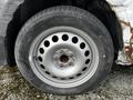 A close-up of a silver steel wheel with multiple circular cutouts mounted on a black tire showing tread wear