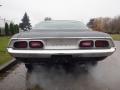 A 1974 Dodge Challenger with a sleek rear design featuring dual taillights and the Dodge emblem positioned prominently on the trunk. The vehicle is partially emitting exhaust.