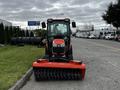 A red 2018 Kubota B2650 tractor with a front-mounted brush attachment parked on a street