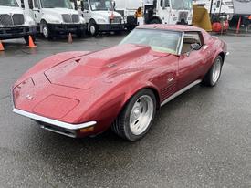 A red 1970 Chevrolet Corvette with a distinctive hood scoop and large wheels sits on a wet surface