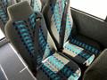 Rows of gray seats with blue and turquoise striped patterns and seat belts in a Blue Bird BB Conventional bus interior